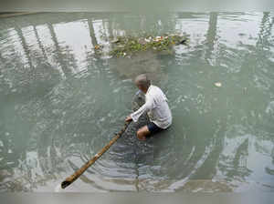 New Delhi: A man cleans a polluted canal for 'Chhath Puja' celebrations, in New ...
