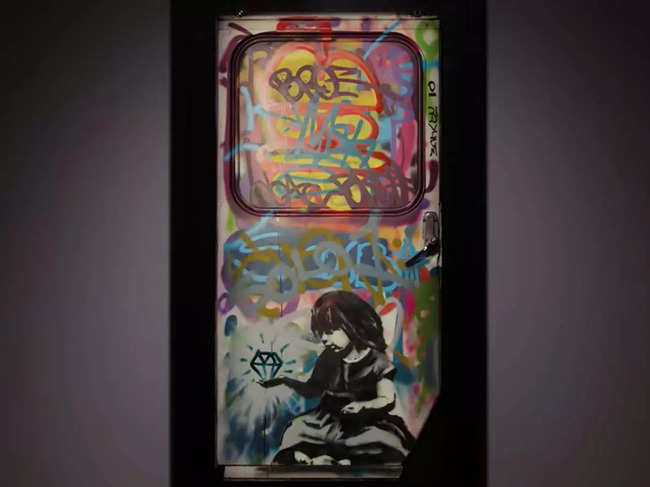 Painted on a steel and glass truck door, Diamond In The Rough employs extant graffiti as the backdrop for a young girl rendered in Banksy’s signature stencil mode, positioned at the bottom of the frame.