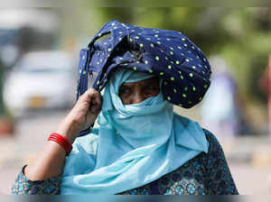 A woman uses her bag to protect herself from the sun, on a hot summer day, in New Delhi
