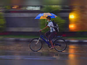 Bengaluru: A boy holds an umbrella as he rides a bi-cycle during heavy rain in B...