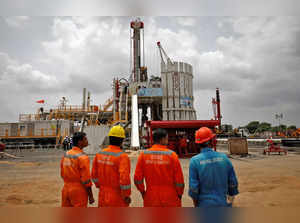 FILE PHOTO: Technicians stand next to an oil rig at an Oil and Natural Gas Corp (ONGC) plant, during a media tour of the plant in Dhamasna