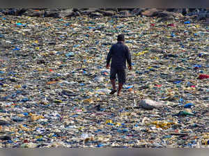 Mumbai: People walk on plastic waste carried by sea waves on coast of Badhwar Pa...