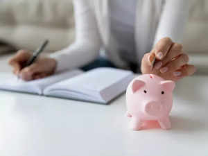 thrifty-woman-writing-daily-expenses-put-coin-into-piggy-bank-picture-id1251273788