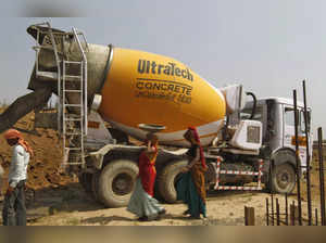 Workers walk in front of an UltraTech concrete mixture truck at the construction site of a commercial complex on the outskirts of  Ahmedabad