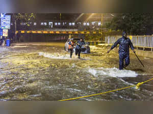 Mumbai: People wade through a waterlogged road as their vehicle gets stuck durin...