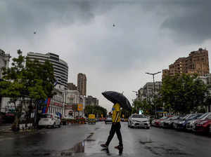 New Delhi: A pedestrian with an umbrella as monsoon clouds hover in the sky, in ...