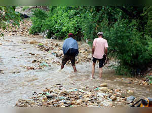 Jammu, July 14 (ANI): People walk through the waterlogged road at Trikuta Nagar ...