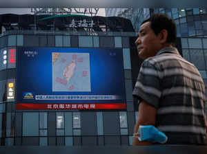 A man stands in front of a screen showing a CCTV news broadcast, featuring a map of locations around Taiwan where Chinese People's Liberation Army (PLA) will conduct military exercises.
