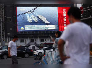 Pedestrians walk past a screen showing footage of Chinese People's Liberation Army (PLA) ships during an evening news programme, in Beijing