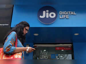 A woman checks her mobile phone as she walks past a mobile store of Reliance Industries' Jio telecoms unit in Mumbai