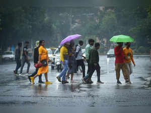 New Delhi: People holding umbrellas cross a road during rains, in New Delhi. (PT...