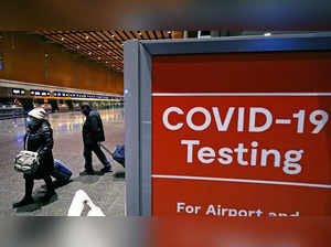 FILE - Travelers pass a sign near a COVID-19 testing site in Terminal E at Logan...