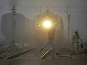 Gurugram: People cross a railway track as a train approaches amid low visibility...