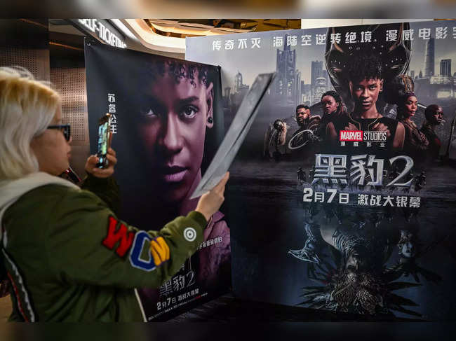 A young woman takes a picture of a poster before watching the movie "Black Panther: Wakanda Forever" at a cinema in Shanghai on February 6, 2023.  Black Panther will be released in Chinese theaters after two and a half year hiatus for Marvel movies. (Photo by Hector RETAMAL / AFP)