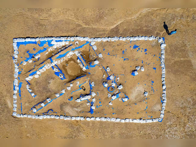 This aerial picture shows Iraqi archaeologist Baqer Azab Wali standing by the newly-excavated trench at the site of the ancient city-state of Lagash, in Iraq's al-Shatra district of the southern Dhi Qar province on February 11, 2023. Italian and US archaeologists excavating in Lagash in southern Iraq have unearthed a Sumerian "tavern" old nearly 5,000 years old, complete with benches, a cooling system acting as a refrigerator, and bowls containing leftover food. (Photo by Asaad NIAZI / AFP)