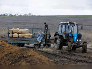 Workers ride in the back of a tractor carrying coffins at a cemetery outside Mariupol