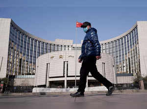 FILE PHOTO: Man wearing a mask walks past the headquarters of the People's Bank of China, the central bank, in Beijing