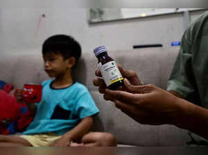This picture taken on February 11, 2023 shows Riski Agri (R) displaying a bottle of cough syrup that was consumed by his son Farrazka which caused him kidney problems, at their house in Jakarta. Five-year-old Farrazka was required to undergo dialysis for his failing kidneys after he took the medicines, his mother Indah Septian told AFP. - To go with "Indonesia-pharmaceutical-children-health", FOCUS by Gemma CAHYA (Photo by BAY ISMOYO / AFP) / To go with "Indonesia-pharmaceutical-children-health", FOCUS by Gemma CAHYA