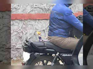 Barbie Doll attached to man's bike pillion seat by black string