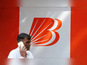 A man talks on mobile phone in front of the Bank of Baroda logo in New Delhi