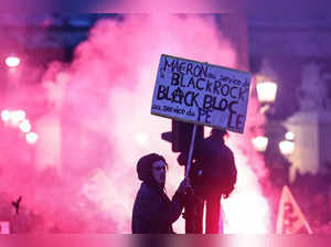 A protester on a traffic light holds a placard reading "Macron at the service of Black Rock, Black bloc at the service of the people" during a demonstration on Place de la Concorde after the French government pushed a pensions reform through parliament without a vote, using the article 49,3 of the constitution, in Paris on March 16, 2023. The French president on March 16 rammed a controversial pension reform through parliament without a vote, deploying a rarely used constitutional power that risks inflaming protests. The move was an admission that his government lacked a majority in the National Assembly