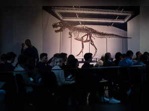 Biders sit next to a picture of 'Trinity' during the sale of the Tyrannosaurus-Rex (T-Rex) skeleton by Koller auction house in Zurich, on April 18, 2023. The T-Rex's skeleton, dating back 67 million years and made up of bones from three dinosaurs excavated between 2008 and 2013 from the Hell Creek and Lance Creek formations in Montana and Wyoming, is expected to fetch six to eight million Swiss francs ($6.5-8.7 million). (Photo by Fabrice COFFRINI / AFP)